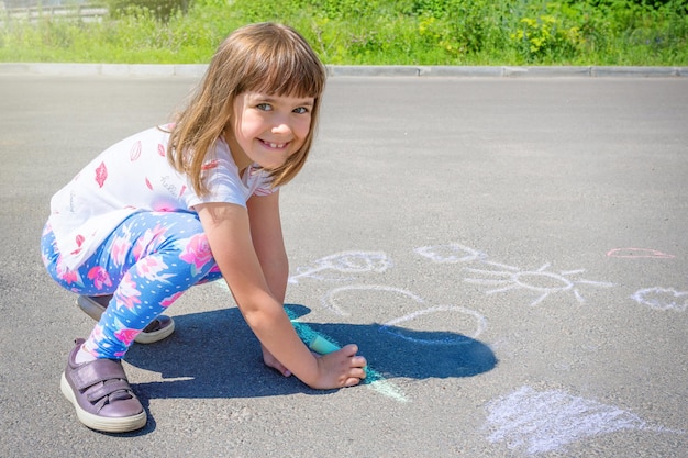 Una linda niña dibuja tizas de colores sobre asfalto Dibujo infantil