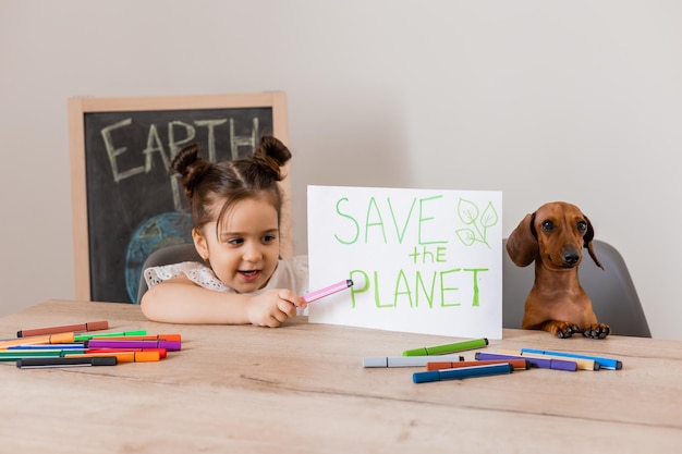 Una linda niña dibujó un letrero que decía "salva el planeta" con su perro salchicha