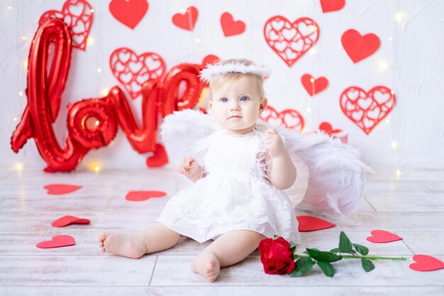 Una linda niña disfrazada de ángel con alas sobre un fondo de corazones rojos y la inscripción ama el concepto del día de san valentín día de san valentín