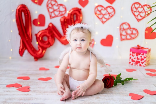 una linda niña disfrazada de ángel con alas sobre un fondo de corazones rojos y la inscripción amor. el concepto de día de san valentín, día de san valentín