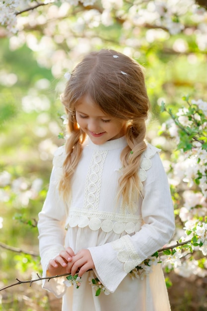 una linda niña divertida con un vestido en primavera cerca de un árbol en flor se ríe de una fotografía suave