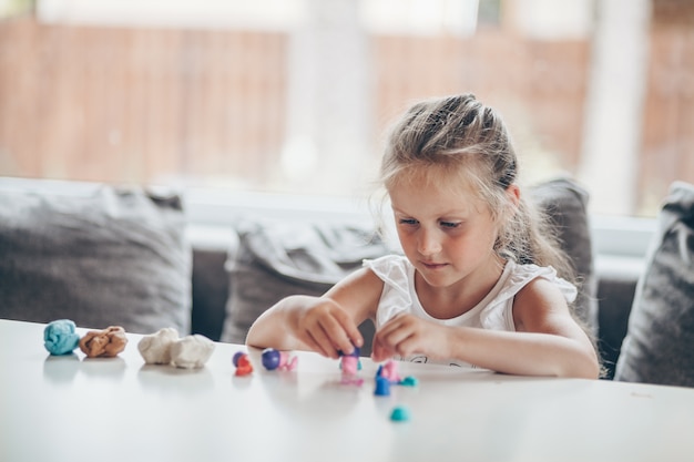 Linda niña en edad preescolar jugando juegos educativos con figuras de plastilina preparándose para la escuela en el jardín de infantes