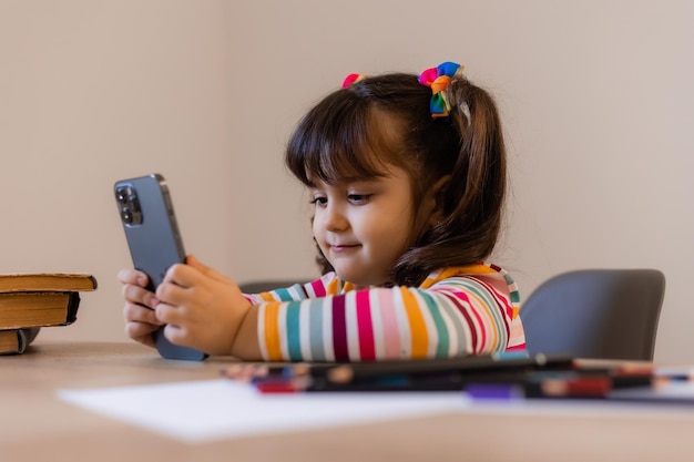 Una linda niña está comprometida con un maestro en línea por teléfono Educación en línea de niños Preescolares y aparatos