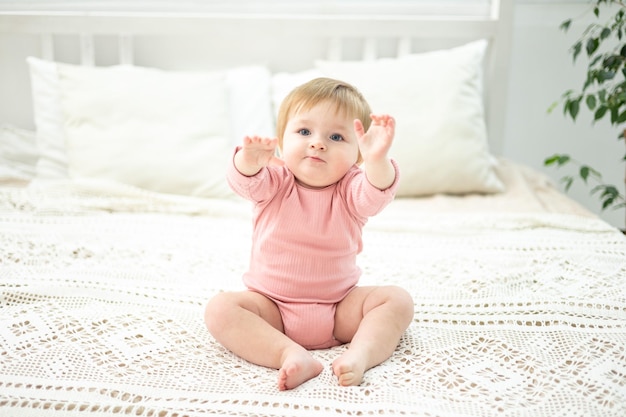 Una linda niña está sentada en una cama con sábanas blancas en el dormitorio de la casa. El retrato de un niño mira a la cámara.