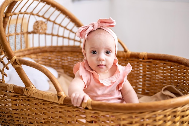 Foto una linda niña europea con ojos marrones en un traje rosa en una cuna de mimbre para niños en la habitación de los niños en casa