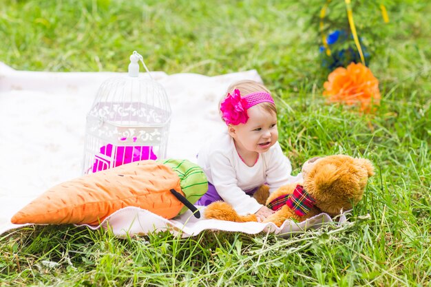 Linda niña feliz con gran oso de peluche marrón en el prado de hierba verde, temporada de primavera o verano.