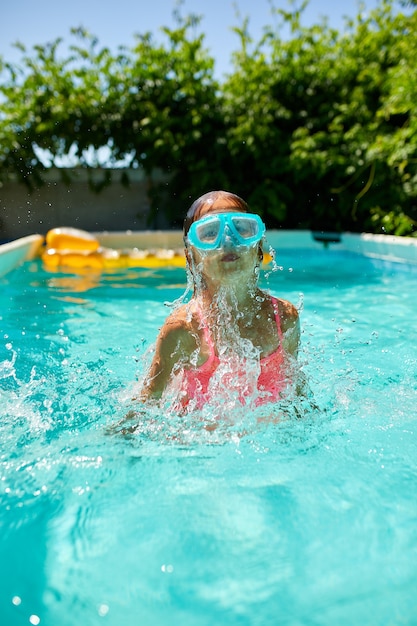 Una linda niña feliz jugando en la piscina con máscara de buceo azul, se sumerge en el agua, vacaciones de verano en casa.