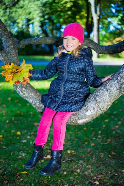 linda niña feliz sentada en la rama de un árbol en el parque de otoño