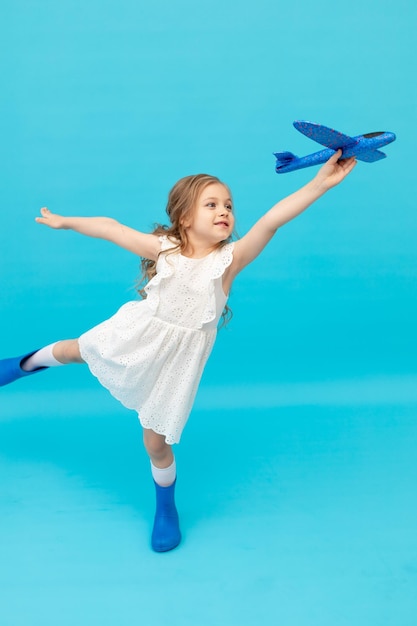 Linda niña feliz con un vestido blanco de algodón en un fondo azul con un avión en sus manos jugando un lugar para el texto