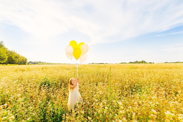 Linda niña con globos está saltando sobre un campo amarillo Cel