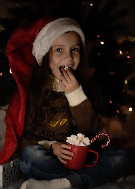 Una linda niña con un gorro de Papá Noel con una taza de cacao