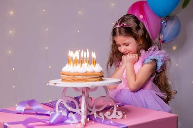 Linda niña con un hermoso vestido pide un deseo y sopla las velas en el pastel de cumpleaños