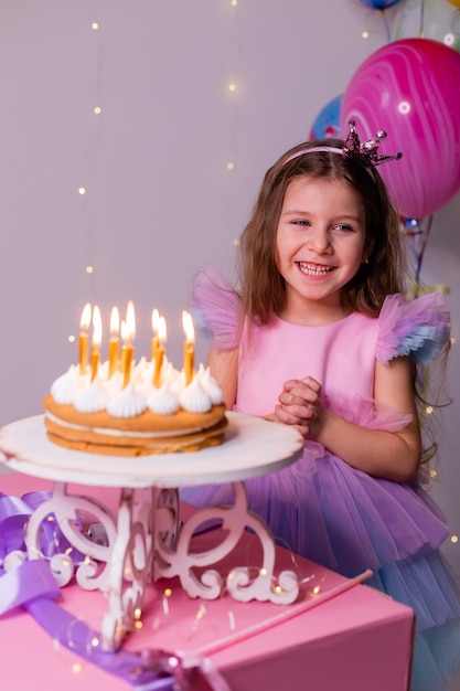 Linda niña con un hermoso vestido pide un deseo y sopla las velas en el pastel de cumpleaños