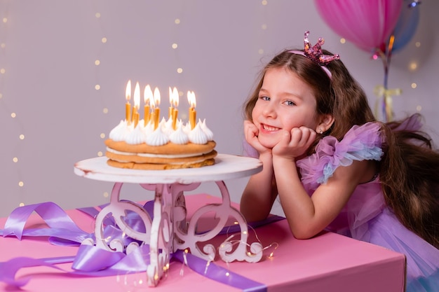 Linda niña con un hermoso vestido pide un deseo y sopla las velas en el pastel de cumpleaños