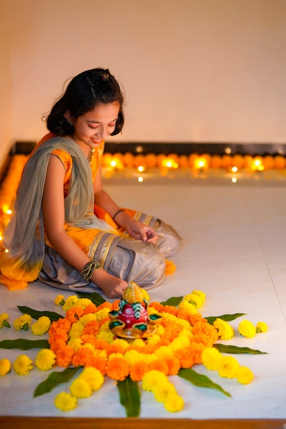 Linda niña india haciendo decoración con flor y lámpara de aceite para el festival de diwali en casa.