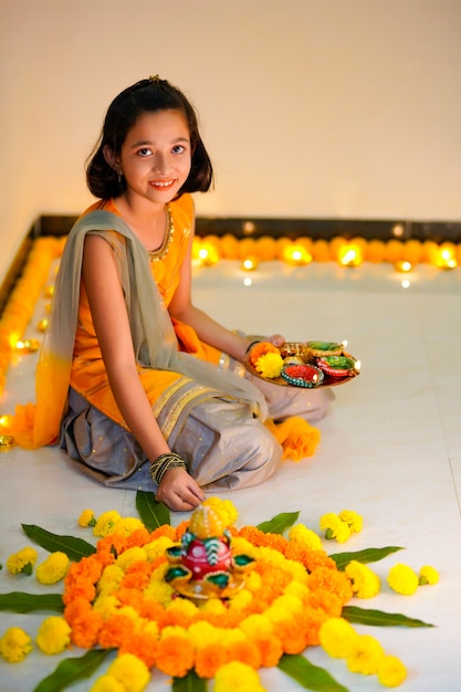 Linda niña india haciendo decoración con flor y lámpara de aceite para el festival de diwali en casa.