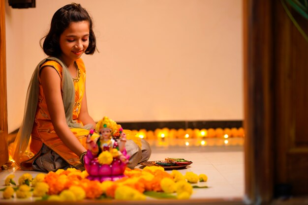 Linda niña india haciendo decoración con flor y lámpara de aceite para el festival de diwali en casa.