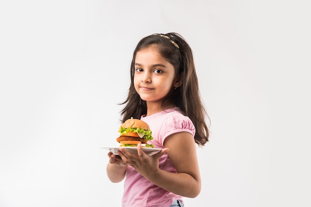 Linda niña india o asiática comiendo hamburguesas sobre fondo blanco.