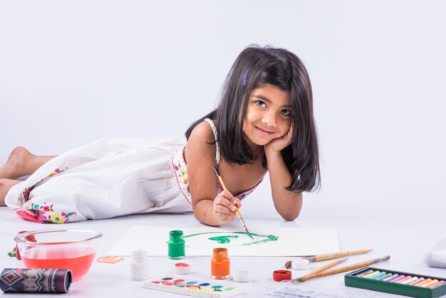 Linda niña india o asiática disfrutando de pintar en casa con papel, acuarela y pincel de arte. Enfoque selectivo