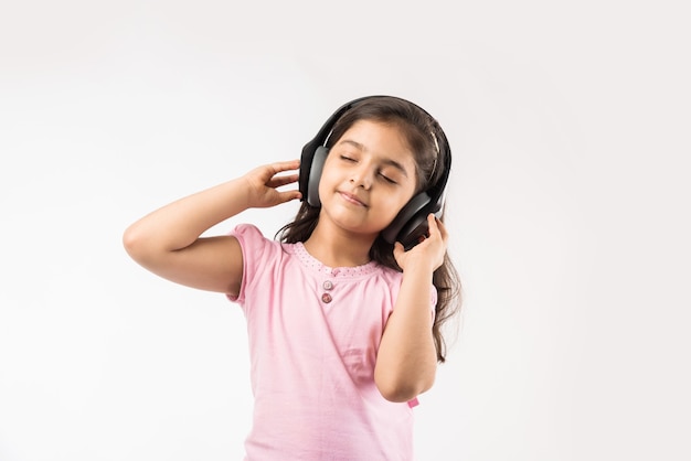 Linda niña india o asiática escuchando música con auriculares inalámbricos aislados en blanco