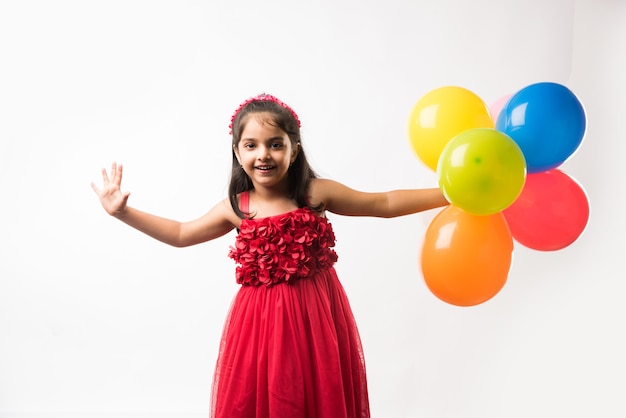 Linda niña india o asiática con globos de colores o gubbare en hindi, sobre fondo blanco o rojo