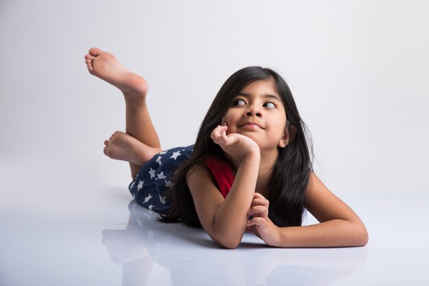 Linda niña india tendida en el suelo con la cabeza apoyada en las manos, aislado sobre fondo blanco.