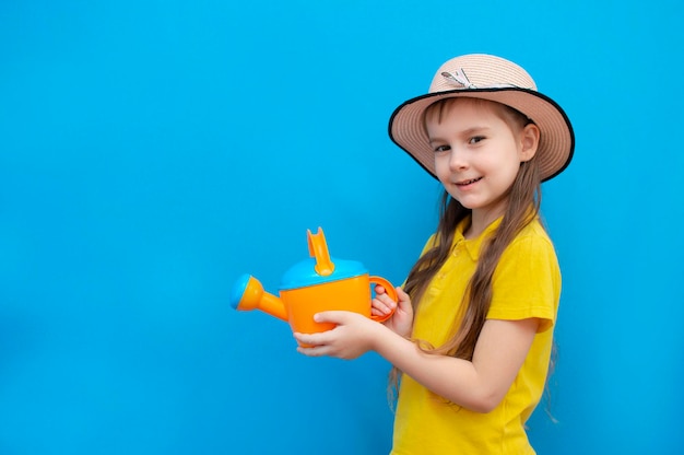 Linda niña jardinera en un sombrero con herramientas de jardinería y en sus manos sobre un fondo azul El niño se está preparando para trasplantar una flor La niña es una jardinera feliz