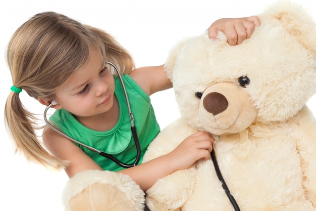 Linda niña jugando al doctor con su oso de peluche