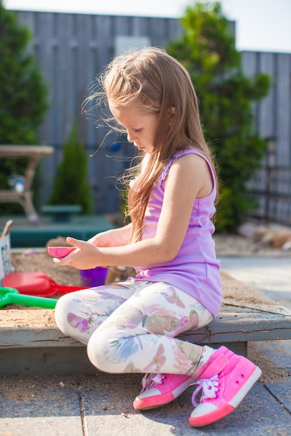 Linda niña jugando en el arenero con juguetes en el patio
