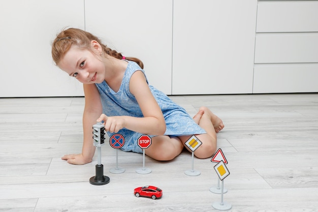 Una linda niña jugando en casa en el suelo con una máquina de escribir, señales de tráfico y semáforos