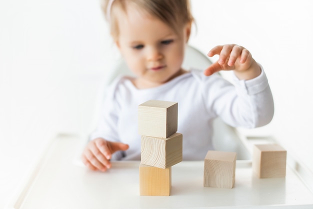 Linda niña jugando con cubos de madera. Torre de construcción de niño pequeño. Bloque de construcción para niños. Método educativo Montessori. Enfoque selectivo