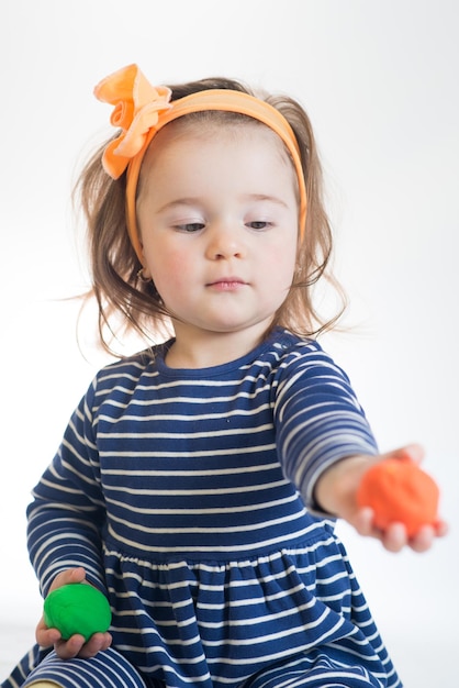 Linda niña jugando con plastilina de colores sobre un fondo blanco.
