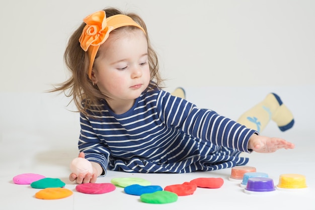 Linda niña jugando con plastilina de colores sobre un fondo blanco.