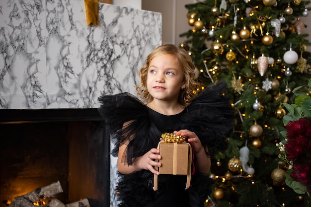 Foto linda niña jugando con regalo de navidad en sus manos y árboles de navidad feliz navidad y felices fiestas