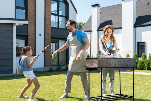 Linda niña jugando con su padre mientras les ayuda a preparar la barbacoa