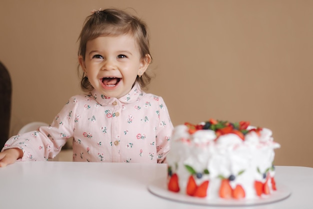 Una linda niña de uno y medio años de edad se encuentra junto a un delicioso pastel de cumpleaños Una niña de dieciocho meses muy feliz y se ríe