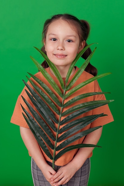 Foto una linda niña mira a la cámara a través del follaje de un árbol tropical y sonríe. aislado en una pared verde.