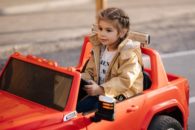 Linda niña monta en una mini ciudad en un coche eléctrico rojo jeep adorable niña camino en juguete