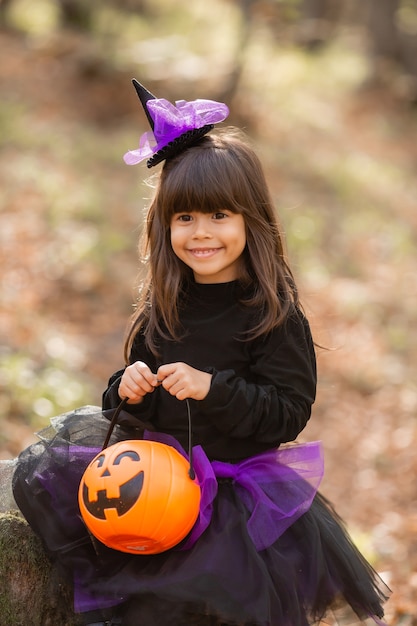 Linda niña morena en un disfraz de bruja de Halloween tiene una canasta de calabaza en sus manos
