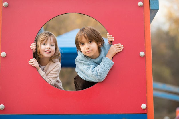 linda niña y niño en el parque infantil divirtiéndose y alegrándose mientras juega en el patio de recreo en el día nublado de otoño