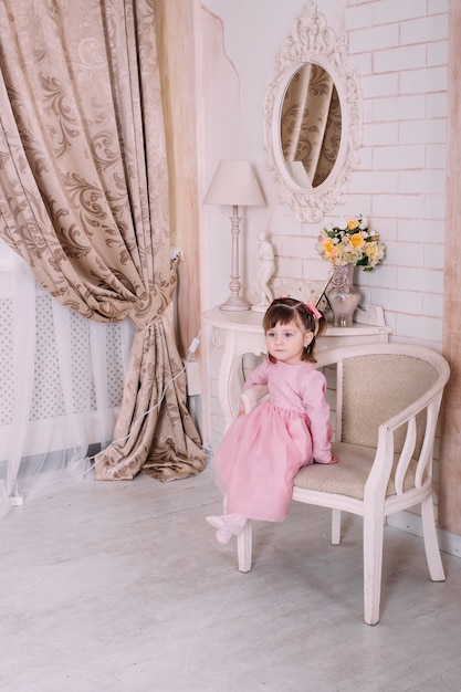 Linda niña niño sentado en una silla con vestido rosa en casa