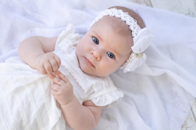 Linda niña con ojos azules en ropa blanca acostada de espaldas sobre un fondo blanco mirando a la cámara