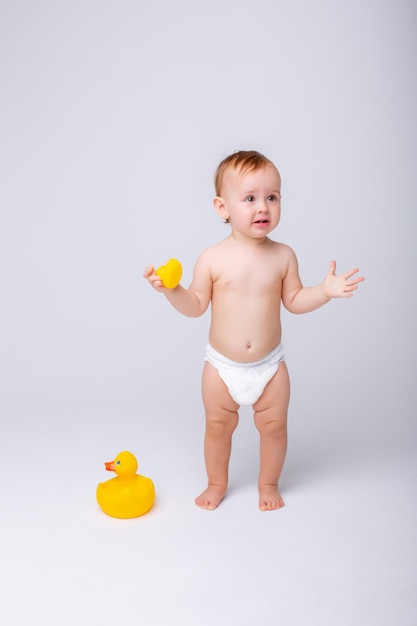 Linda niña en un pañal jugando con un pato de juguete de goma aislado sobre un fondo blanco.