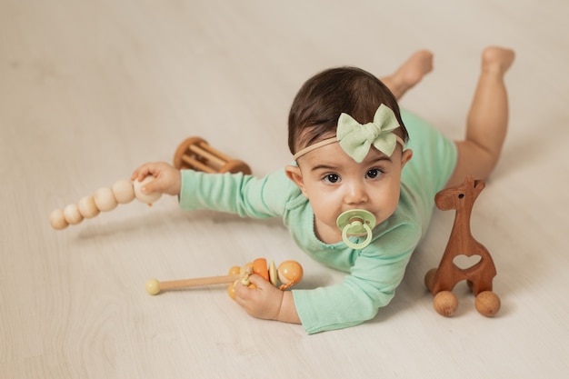 Linda niña pequeña de 8 meses se encuentra en el piso de madera de la casa jugando con juguetes de desarrollo de madera. Foto de alta calidad