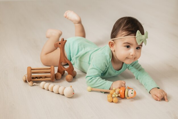 Linda niña pequeña de 8 meses se encuentra en el piso de madera de la casa jugando con juguetes de desarrollo de madera. Foto de alta calidad