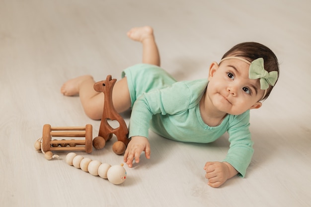 Linda niña pequeña de 8 meses se encuentra en el piso de madera de la casa jugando con juguetes de desarrollo de madera. Foto de alta calidad