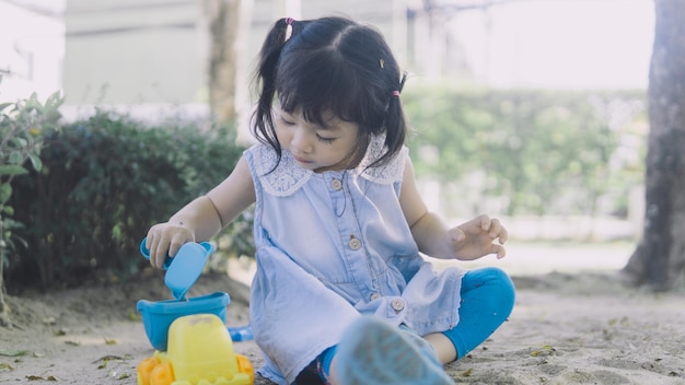 Linda niña pequeña asiática jugando en la arena en el patio de recreo al aire libre
