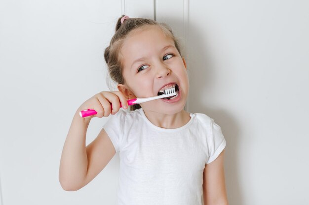 Linda niña pequeña se cepilla los dientes con un cepillo de dientes rosa. Fondo blanco. Salud dental.