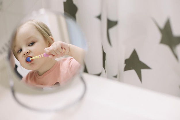 Linda niña pequeña cepillarse los dientes en el baño Limpieza de dientes cuidado dental