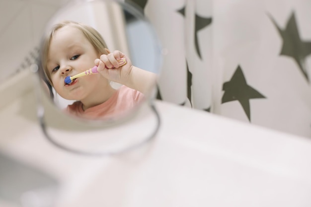 Linda niña pequeña cepillarse los dientes en el baño Limpieza de dientes cuidado dental